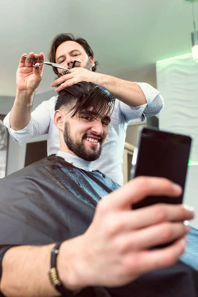 Hombres Una Peluquería Usando Teléfono Inteligente Mientras Tienen Corte Pelo —  Fotos de Stock