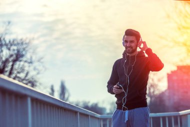 Günbatımında akıllı telefon ve kulaklıkla koşan bir adam.
