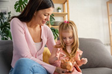 Genç anne kumbarayı elinde tutarken tatlı kızıyla evde oturuyor. 