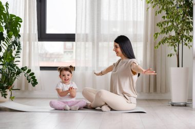 Anne küçük kızıyla evde yoga yapıyor.