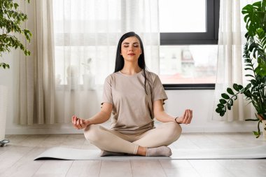 Spor kıyafetli güzel bir kız evde yoga yapıyor. 