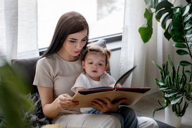 Mutlu anne ve kız evde kitap okuyor.