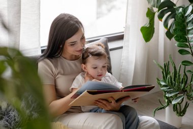 Mutlu anne ve kız evde kitap okuyor.