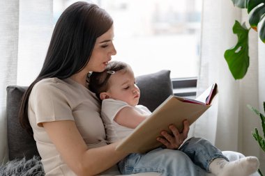 Mutlu anne ve kız evde kitap okuyor.