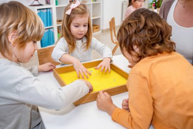 Cheerful children playing with a play sand in the kindergarten clipart