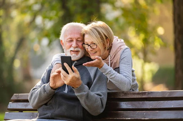 elderly couple using mobile phone sitting on the bench in park