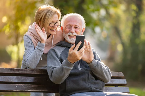 elderly couple using mobile phone sitting on the bench in park