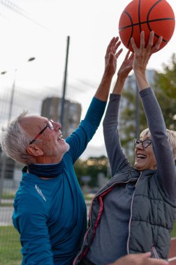Yaşlı kadın ve olgun erkek parkta basketbol oynuyorlar.