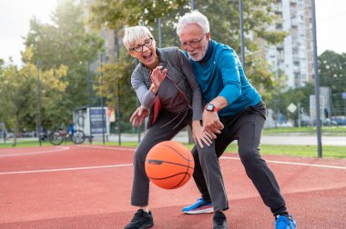 Yaşlı kadın ve olgun erkek parkta basketbol oynuyorlar.
