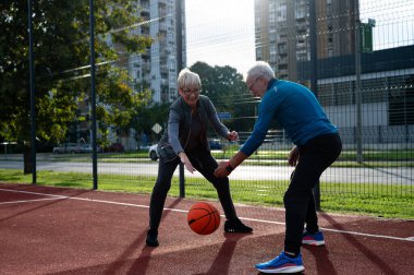 Yaşlı kadın ve olgun erkek parkta basketbol oynuyorlar.