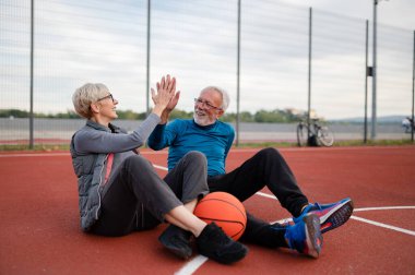 Yaşlı kadın ve olgun erkek parkta basketbol oynuyorlar.