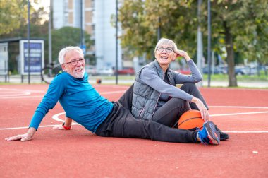 Yaşlı kadın ve olgun erkek parkta basketbol oynuyorlar.