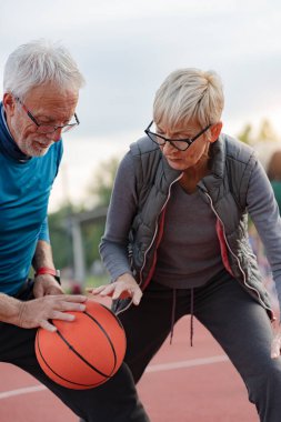 Yaşlı kadın ve olgun erkek parkta basketbol oynuyorlar.