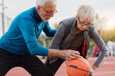 Yaşlı kadın ve olgun erkek parkta basketbol oynuyorlar.