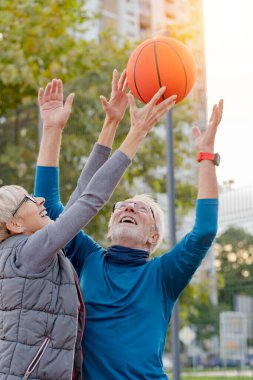 Yaşlı kadın ve olgun erkek parkta basketbol oynuyorlar.