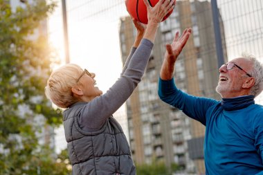 Yaşlı kadın ve olgun erkek parkta basketbol oynuyorlar.