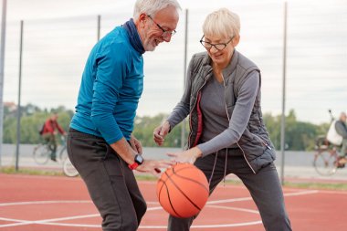 Yaşlı kadın ve olgun erkek parkta basketbol oynuyorlar.