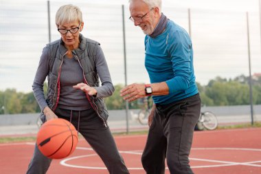 Yaşlı kadın ve olgun erkek parkta basketbol oynuyorlar.