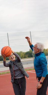 Yaşlı kadın ve olgun erkek parkta basketbol oynuyorlar.