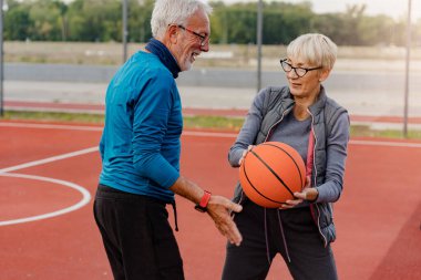 Yaşlı kadın ve olgun erkek parkta basketbol oynuyorlar.