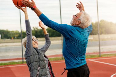 Yaşlı kadın ve olgun erkek parkta basketbol oynuyorlar.