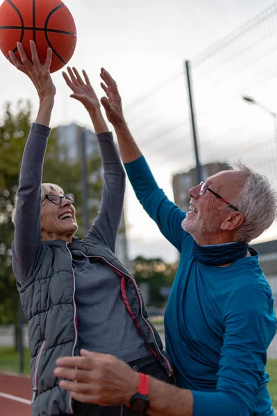 Yaşlı kadın ve olgun erkek parkta basketbol oynuyorlar.