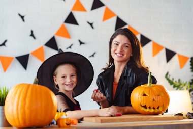 Mutlu anne ve kız Cadılar Bayramı 'na hazırlanıyor, anne ve kız çocukları yüzlerini boyuyor.