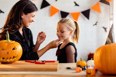 Mutlu anne ve kız Cadılar Bayramı 'na hazırlanıyor, anne ve kız çocukları yüzlerini boyuyor.