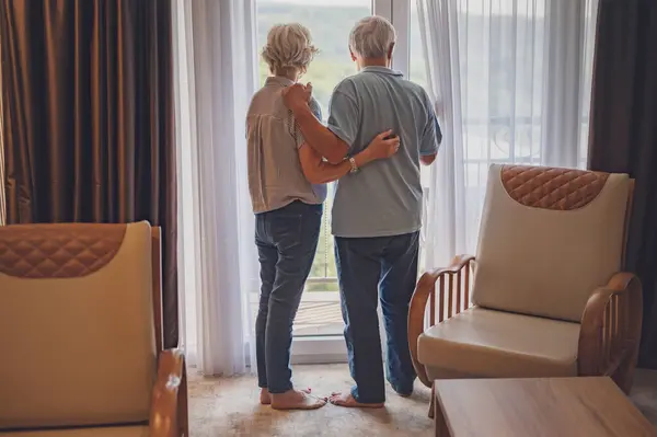 一对上了年纪的已婚夫妇刚刚来到旅馆 从他们豪华公寓的窗户往外看 — 图库照片