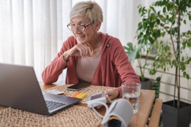 Evde dizüstü bilgisayarın önünde oturan yaşlı bir kadın bir doktorla görüntülü görüşme yapıyor. Online tıbbi danışmanlık
