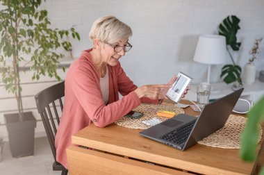 Evde dizüstü bilgisayarın önünde oturan yaşlı bir kadın bir doktorla görüntülü görüşme yapıyor. Online tıbbi danışmanlık