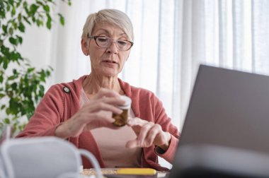 Evde dizüstü bilgisayarın önünde oturan yaşlı bir kadın bir doktorla görüntülü görüşme yapıyor. Online tıbbi danışmanlık