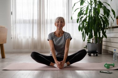 İçeride yoga yapan aktif son sınıf öğrencisi bir kadın.