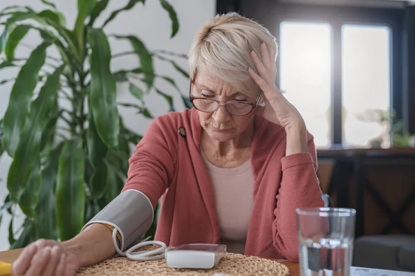 Senior woman sitting alone at home, measuring her blood pressure with a home device