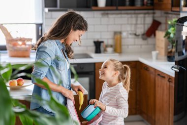 Anne ve kızı öğle yemeğini okul çantasına koyuyorlar.