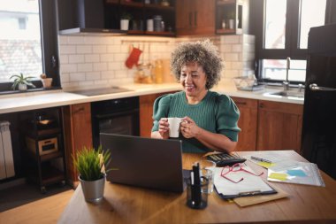 Mutfakta dizüstü bilgisayar kullanan son sınıf kadın serbest yazar.  