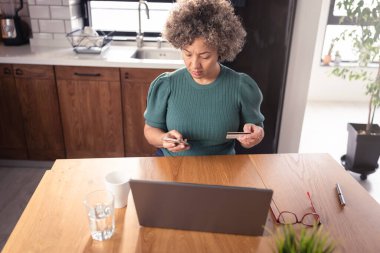 Kredi kartıyla ödeme yaparken dizüstü bilgisayar kullanan yaşlı bir kadın. 