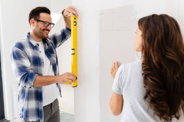 Bir adam ve hamile karısından oluşan genç, güzel ve neşeli bir çift, yeni ev yenileme projesinin bir parçası olarak duvarları ölçüyorlar.