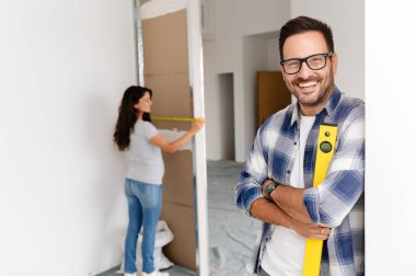 Bir adam ve hamile karısından oluşan genç, güzel ve neşeli bir çift, yeni ev yenileme projesinin bir parçası olarak duvarları ölçüyorlar.