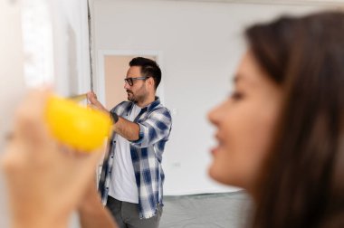 Bir adam ve hamile karısından oluşan genç, güzel ve neşeli bir çift, yeni ev yenileme projesinin bir parçası olarak duvarları ölçüyorlar.