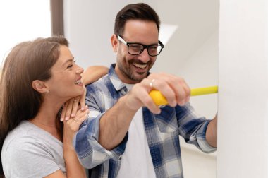 Bir adam ve hamile karısından oluşan genç, güzel ve neşeli bir çift, yeni ev yenileme projesinin bir parçası olarak duvarları ölçüyorlar.