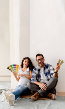 Hamile kadın ve kocası yeni dairenin duvarlarını boyamak için boya rengi seçiyorlar.