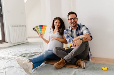 Hamile kadın ve kocası yeni dairenin duvarlarını boyamak için boya rengi seçiyorlar.