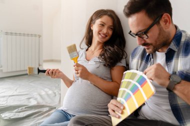 Hamile kadın ve kocası yeni dairenin duvarlarını boyamak için boya rengi seçiyorlar.