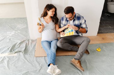 Hamile kadın ve kocası yeni dairenin duvarlarını boyamak için boya rengi seçiyorlar.