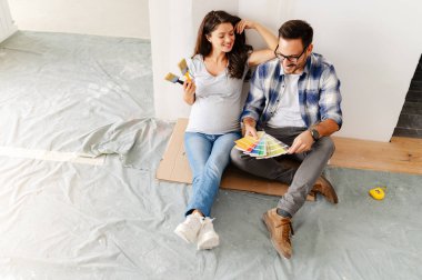 Hamile kadın ve kocası yeni dairenin duvarlarını boyamak için boya rengi seçiyorlar.