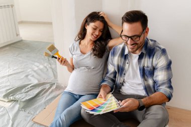 Hamile kadın ve kocası yeni dairenin duvarlarını boyamak için boya rengi seçiyorlar.