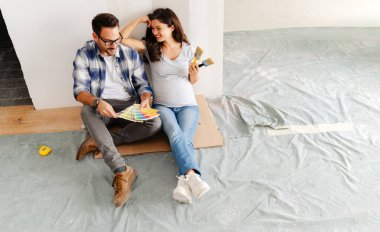 Hamile kadın ve kocası yeni dairenin duvarlarını boyamak için boya rengi seçiyorlar.