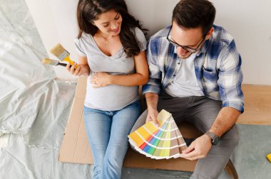 Hamile kadın ve kocası yeni dairenin duvarlarını boyamak için boya rengi seçiyorlar.