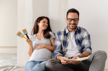 Hamile kadın ve kocası yeni dairenin duvarlarını boyamak için boya rengi seçiyorlar.